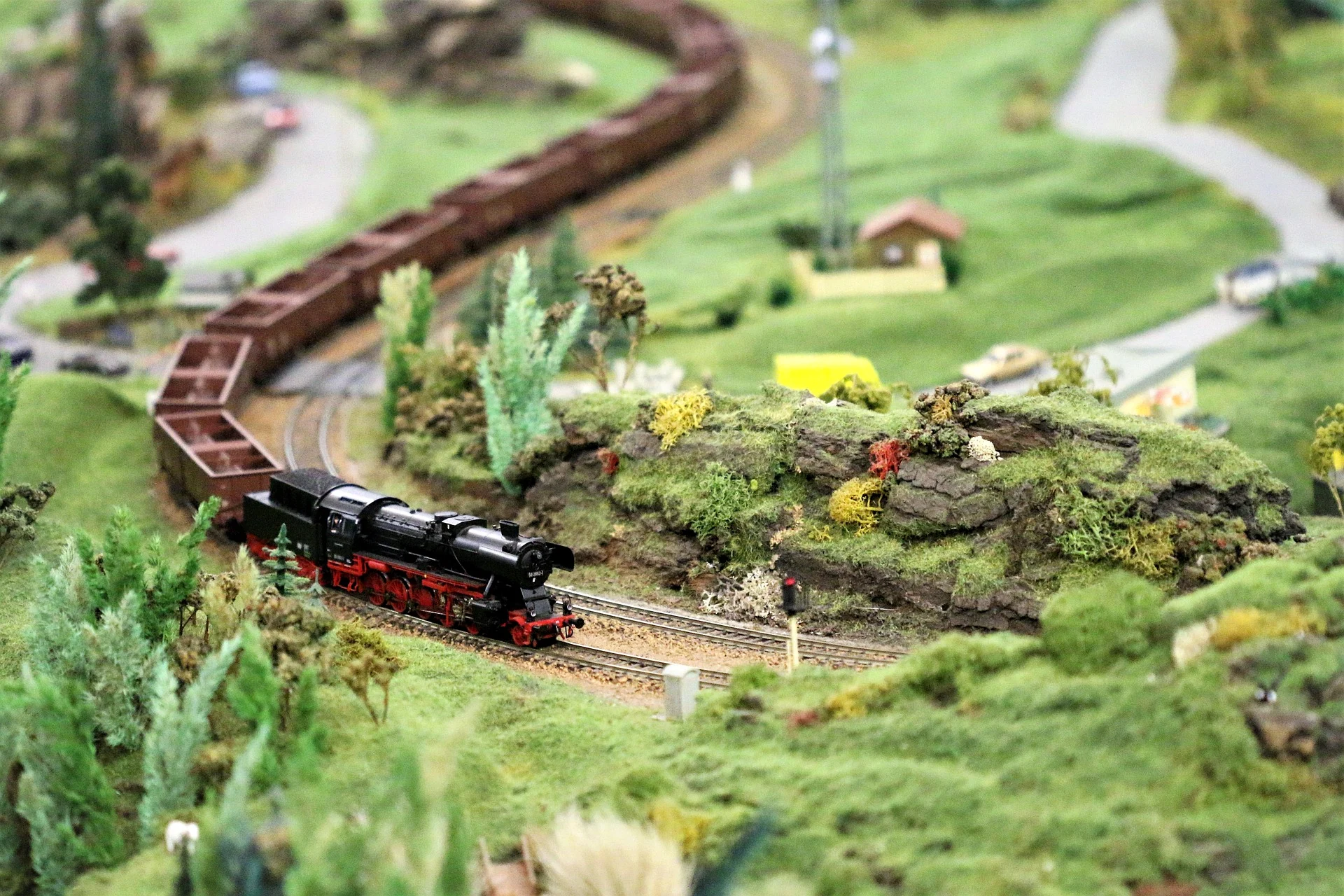 Detailreiche Modellbahnszene mit Dampflokomotive, Landschaft und Straße